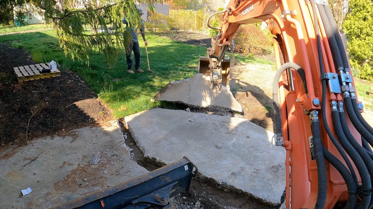 Excavator lifting broken concrete slab pieces out of a yard